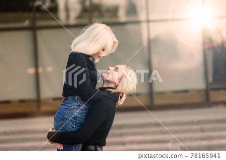 Two young females walking smiling embracing and kissing outdoor in the city 78165941