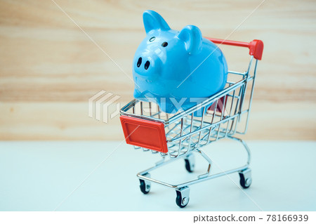 Blue piggy bank in small toy shopping basket on wooden background. Blue piggy bank in small toy shopping basket on wooden background. 78166939