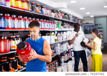Focused muscular man looking for necessary sport nutrition products in shop, reading content label Focused muscular man looking for necessary sport nutrition products in shop, reading content label 78167282