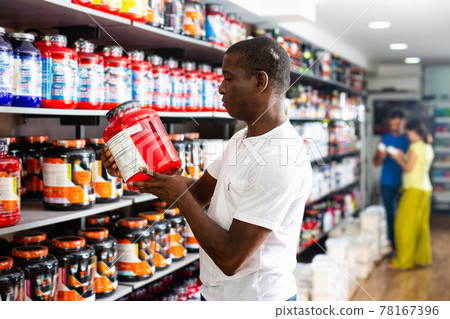 Focused muscular African man choosing sports nutrition products in shop, reading content label Focused muscular African man choosing sports nutrition products in shop, reading content label 78167396