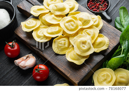 Raw ravioli with ricotta and spinach, on wooden cutting board, on black wooden table background Raw ravioli with ricotta and spinach, on wooden cutting board, on black wooden table background 78168077