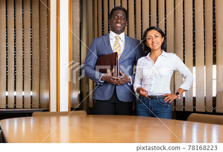 Smiling businessman and businesswoman standing in meeting room Smiling businessman and businesswoman standing in meeting room 78168223