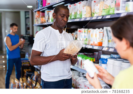 Focused muscular African man choosing sports nutrition products in shop, reading content label Focused muscular African man choosing sports nutrition products in shop, reading content label 78168235