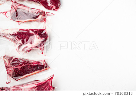 Fresh tasty raw beef steaks with bone wrapped in vacuum plastic packing at market, tomahawk, t bone, club steak, rib eye and tenderloin cuts, on white stone background, top view flat lay, with copy 78168313