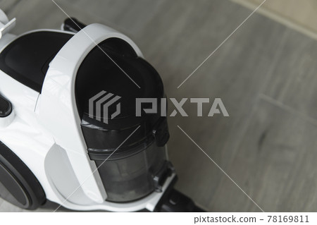 Bagless cyclone vacuum cleaner on a grey tile. Electrical apparatus that by means of suction collects dust and small particles from floors and other surfaces. Bagless cyclone vacuum cleaner on a grey tile. Electrical apparatus that by means of suction collects dust and small particles from floors and other surfaces. 78169811