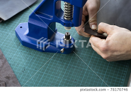 Artisan using hand press for setting snaps in leather for makes a wallet. Hand Pressure Snap Pressing Machine is using by craftsman in leather workshop. 78170746