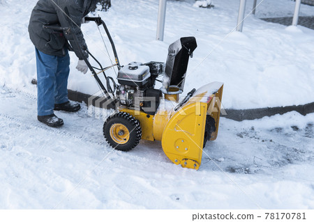 Man cleaning driveway with snow machines after a snow storm. Snow removal equipment working on the street. Cleaning of streets from snow. It's snowing. Man cleaning driveway with snow machines after a snow storm. Snow removal equipment working on the street. Cleaning of streets from snow. It's snowing. 78170781