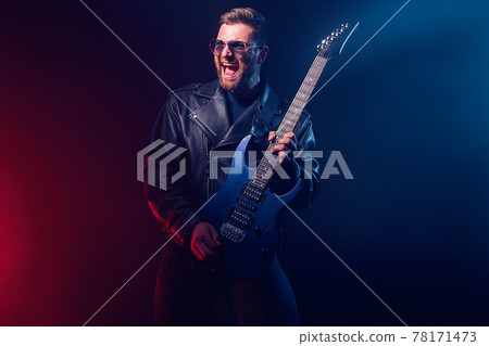 Brutal bearded Heavy metal musician in leather jacket and sunglasses is playing electrical guitar. Shot in a studio on dark background with smoke Brutal bearded Heavy metal musician in leather jacket and sunglasses is playing electrical guitar. Shot in a studio on dark background with smoke 78171473