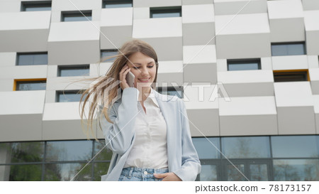 Caucasian Confident Young Business Woman in White Shirt is Talking on Phone Outside near Modern Office Building. Medium Long Low Angle 4K Slow Motion Corporate Shot with Moving Around. Career people 78173157