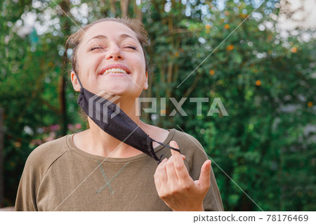 Happy positive girl takes off protective medical mask from face outdoors. Young woman removing mask smiling after vaccination. Coronavirus pandemic Covid 19 concept. Spring flowers pollen allergy. Happy positive girl takes off protective medical mask from face outdoors. Young woman removing mask smiling after vaccination. Coronavirus pandemic Covid 19 concept. Spring flowers pollen allergy. 78176469