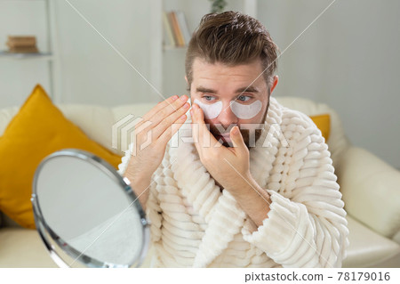 Bearded man applying eye patches on his face. Wrinkles and face home care for men. Bearded man applying eye patches on his face. Wrinkles and face home care for men. 78179016