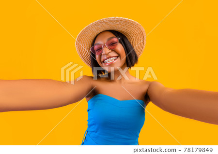 Portrait of joyful African American woman in summer outfit taking selfie on mobile phone over orange studio background Portrait of joyful African American woman in summer outfit taking selfie on mobile phone over orange studio background 78179849