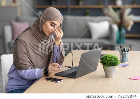 Tired muslim woman sitting at desk, rubbing dry irritated eyes Tired muslim woman sitting at desk, rubbing dry irritated eyes 78179874