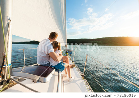 Father And Daughter Sailing On Yacht Sitting On Deck, Back-View 78180019
