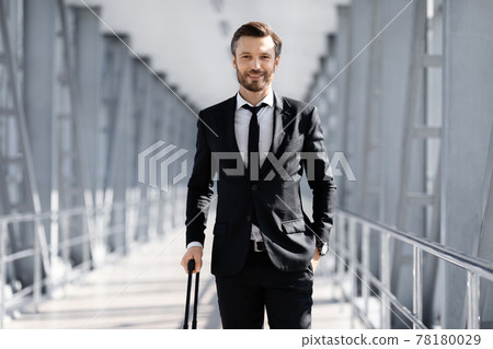 Wealthy manager in black suit with suitcase posing in airport 78180029