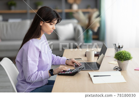 Woman using calculator working on laptop at home 78180030