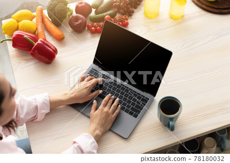 Woman using pc with empty screen for mockup in kitchen 78180032