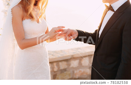 The bride puts the ring on the groom's finger during the wedding ceremony The bride puts the ring on the groom's finger during the wedding ceremony 78182538