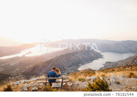 The bride and groom sitting and hugging on the wooden bench on the top of Mount Lovcen overlooking the Bay of Kotor The bride and groom sitting and hugging on the wooden bench on the top of Mount Lovcen overlooking the Bay of Kotor 78182544