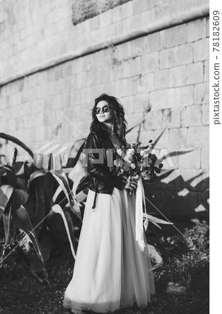 Black and white photo of bride in sunglasses with a bouquet of flowers against the background of the castle wall and agave 78182609