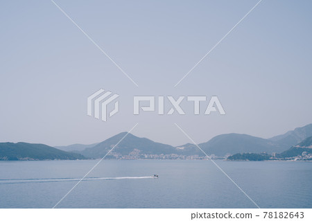 A small motor boat sails on the sea against the backdrop of the Montenegrin coast near Budva and Becici. Minimalistic summer landscape. A small motor boat sails on the sea against the backdrop of the Montenegrin coast near Budva and Becici. Minimalistic summer landscape. 78182643