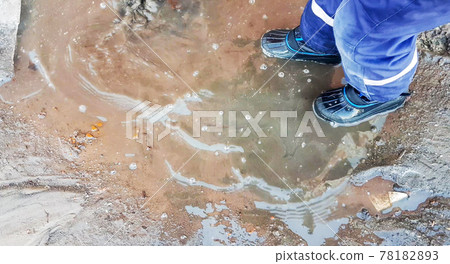 Close-up of a child's feet in rubber boots, a boy child happily playing with a shovel in a muddy puddle with snow and ice, in the early spring in the yard 78182893