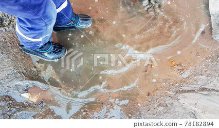 Close-up of a child's feet in rubber boots, a boy child happily playing with a shovel in a muddy puddle with snow and ice, in the early spring in the yard 78182894