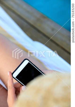 female hand holding a phone - smartphone on the background of a tanned leg on a blue sea lounger female hand holding a phone - smartphone on the background of a tanned leg on a blue sea lounger 78183280