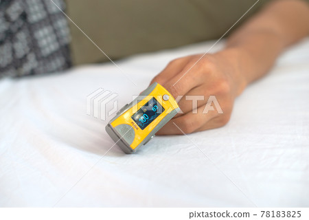 Close-up of woman's hand resting on bed, wearing pulse oximeter to measure blood oxygen saturation 78183825