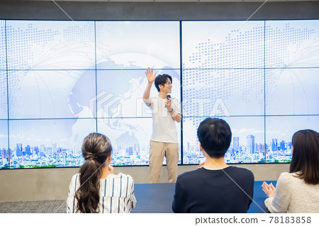 A young man giving a speech in front of a huge monitor A young man giving a speech in front of a huge monitor 78183858