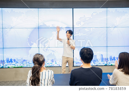 A young man giving a speech in front of a huge monitor A young man giving a speech in front of a huge monitor 78183859