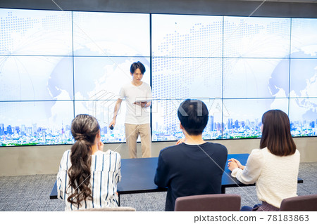 A young man giving a speech in front of a huge monitor A young man giving a speech in front of a huge monitor 78183863