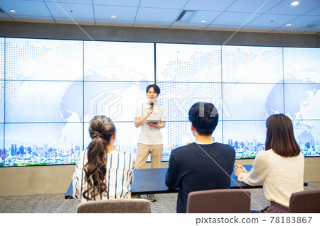 A young man giving a speech in front of a huge monitor A young man giving a speech in front of a huge monitor 78183867