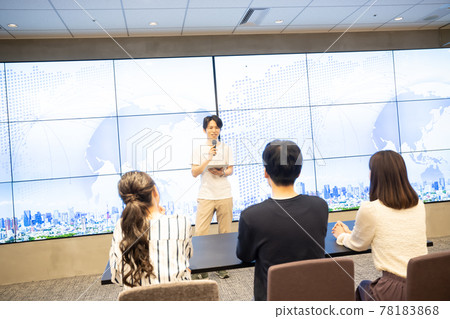 A young man giving a speech in front of a huge monitor A young man giving a speech in front of a huge monitor 78183868