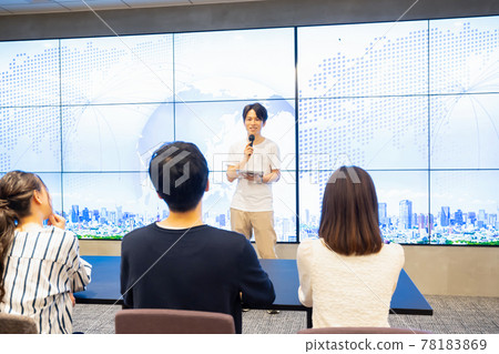 A young man giving a speech in front of a huge monitor A young man giving a speech in front of a huge monitor 78183869