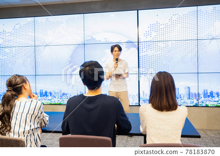 A young man giving a speech in front of a huge monitor A young man giving a speech in front of a huge monitor 78183870