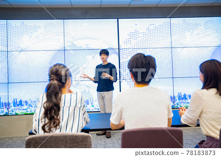 Young man giving a presentation in front of a huge monitor Young man giving a presentation in front of a huge monitor 78183873