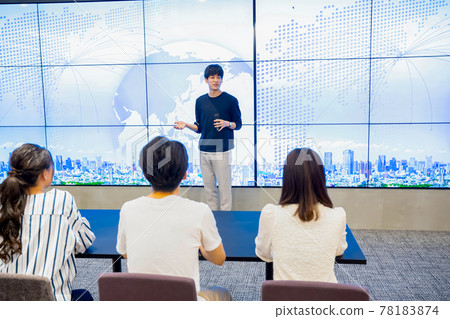 Young man giving a presentation in front of a huge monitor Young man giving a presentation in front of a huge monitor 78183874