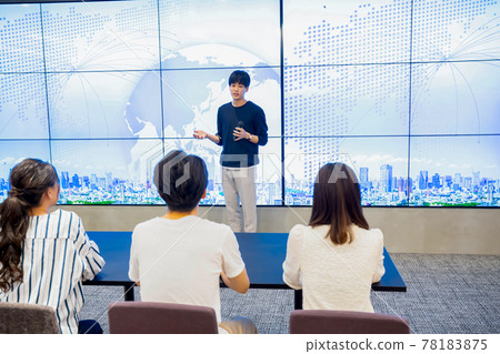Young man giving a presentation in front of a huge monitor Young man giving a presentation in front of a huge monitor 78183875