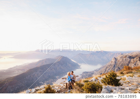 Hugging covered with a blanket couple sits on a bench and drinks tea against the backdrop of a mountain panorama Hugging covered with a blanket couple sits on a bench and drinks tea against the backdrop of a mountain panorama 78183895