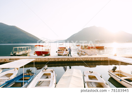 Groom and bride walk along the pier on the coast of the bay past the parked yachts 78183945