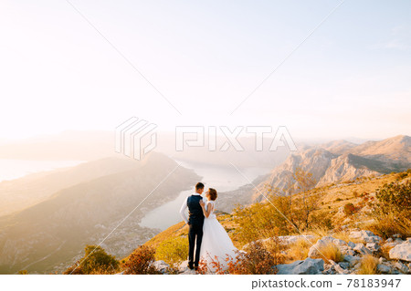 The bride and groom stand on the top of Mount Lovcen overlooking the Bay of Kotor, smile and hug tenderly  78183947