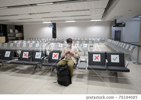 Waiting for flight at empty airport in Cyprus. Man sitting on chair with social distance marker at empty Paphos terminal. Flights canceled during quarantine. Collapse of airlines at coronavirus 78184085