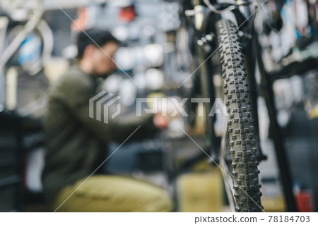 Mechanic repairs bicycle in workshop wearing covid 19 mask. Worker of bicycle store fixes bike during coronavirus quarantine in protective mask. Repairman maintenance cycle. Sport shop concept 78184703