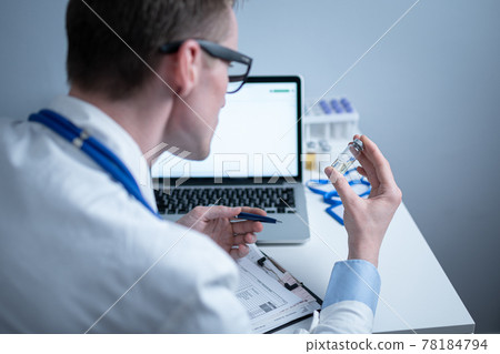 Scientist in medical laboratory examines vial of medicine, vaccine against viruses, influenza, covid. Doctor enters information into computer about investigation. Immunization from terrible diseases Scientist in medical laboratory examines vial of medicine, vaccine against viruses, influenza, covid. Doctor enters information into computer about investigation. Immunization from terrible diseases 78184794
