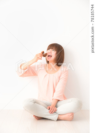 A young woman sitting cross-legged with a snack in one hand A young woman sitting cross-legged with a snack in one hand 78185744