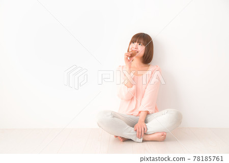 一個年輕女子盤腿坐著,一隻手拿著零食 一個年輕女子盤腿坐著,一隻手拿著零食 78185761