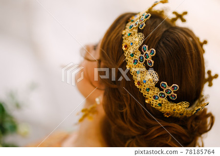 A woman with a beautiful hairstyle in a gold crown with stones, close-up. Bride wearing a crown on an orthodox wedding A woman with a beautiful hairstyle in a gold crown with stones, close-up. Bride wearing a crown on an orthodox wedding 78185764