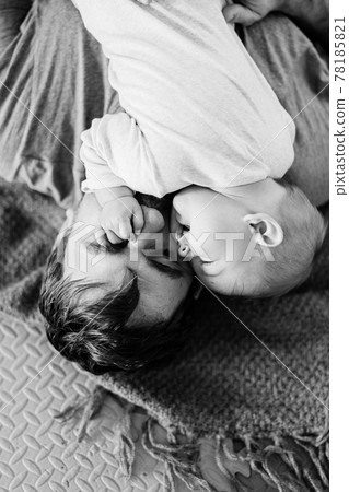 Tiny baby lies on dad's chest with a hand on his face. Black and white photo. Close-up 78185821