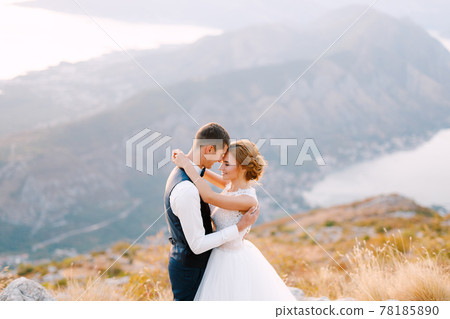 The bride and groom stand on the top of Mount Lovcen overlooking the Bay of Kotor and hug tenderly, close-up The bride and groom stand on the top of Mount Lovcen overlooking the Bay of Kotor and hug tenderly, close-up 78185890